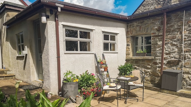 Une petite maison à l’extérieur blanc, avec un mur en pierre et une terrasse comprenant une chaise et une table.