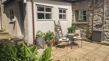 A small house with a white exterior, a stone wall, and a patio area with a chair and table.