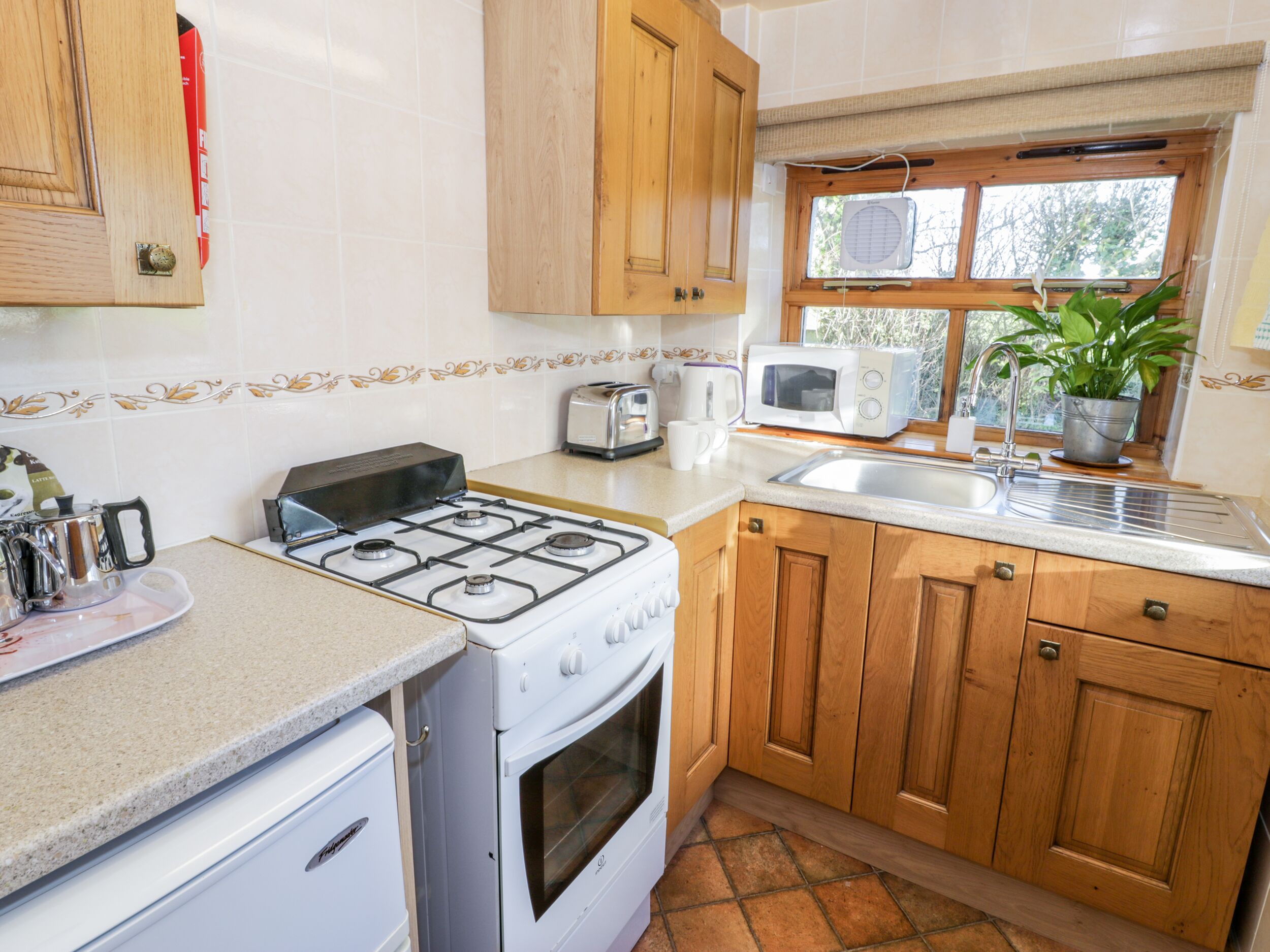 A kitchen with a gas stove, oven, wooden cabinets, a microwave, a sink, and a window with a plant.