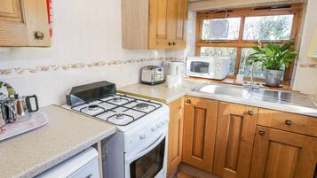 A kitchen with a gas stove, oven, wooden cabinets, a microwave, a sink, and a window with a plant.