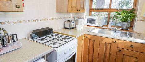 A kitchen with a gas stove, oven, wooden cabinets, a microwave, a sink, and a window with a plant.