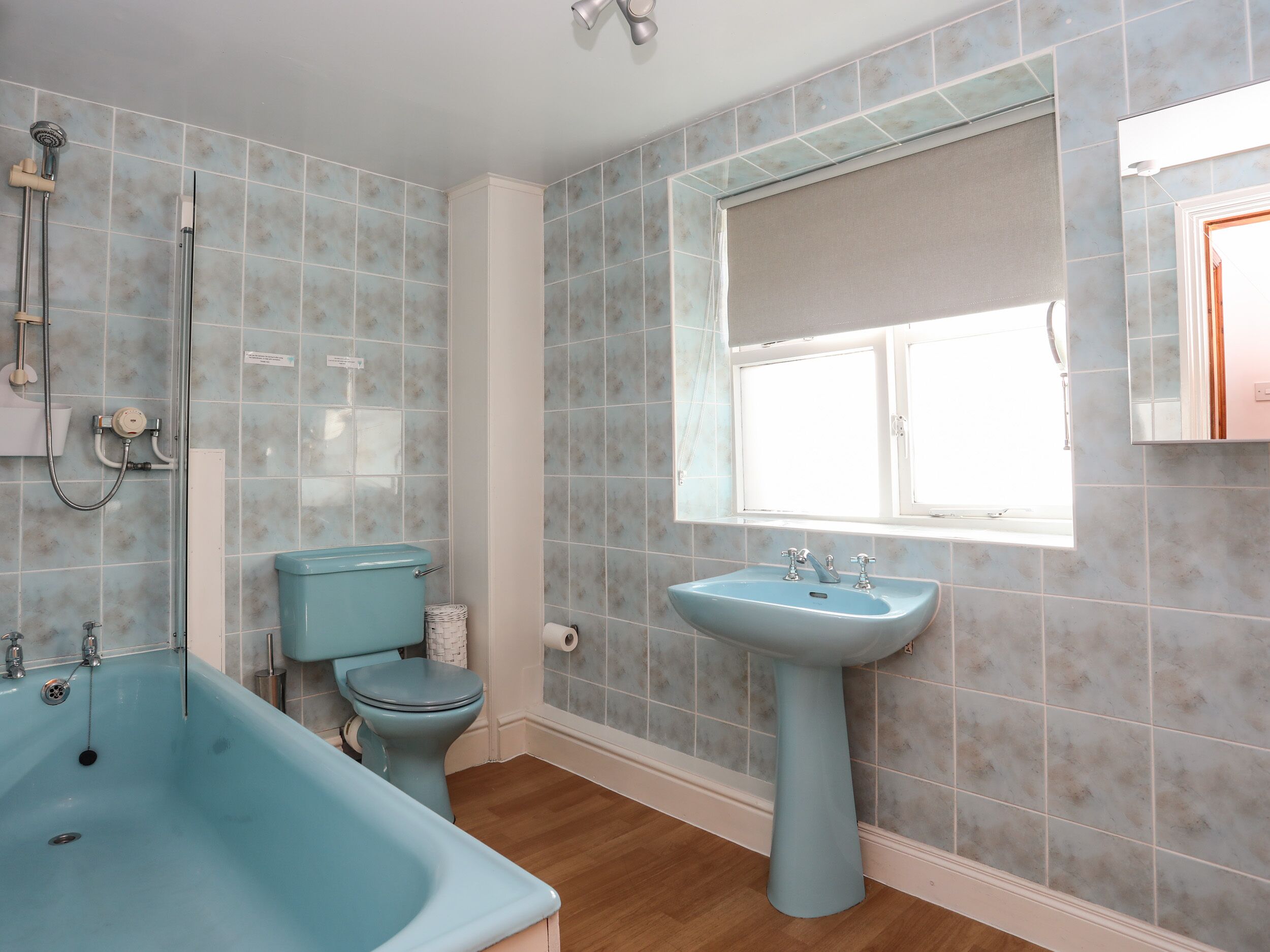 A bathroom with a blue bathtub, toilet, and sink, tiled walls, and a window.