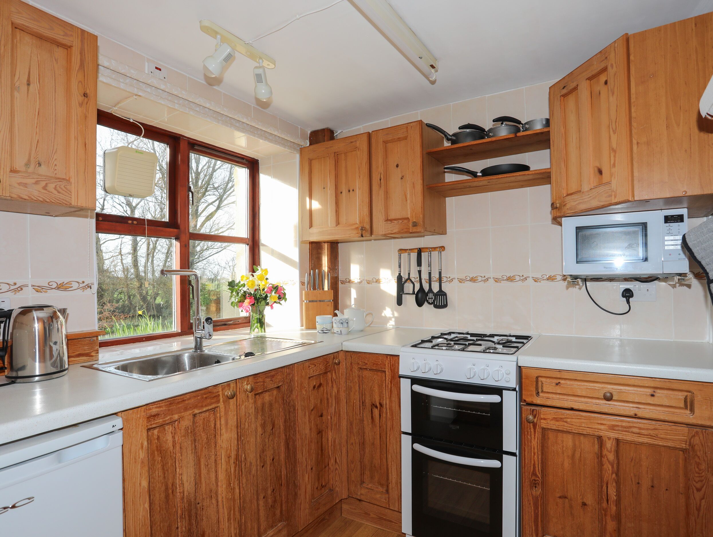 A kitchen with wooden cabinets, a stove, a microwave, and a window with flowers.