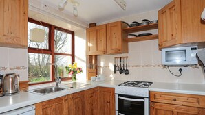 Une cuisine avec des meubles en bois, une cuisinière, un four à micro-ondes et une fenêtre décorée de fleurs.