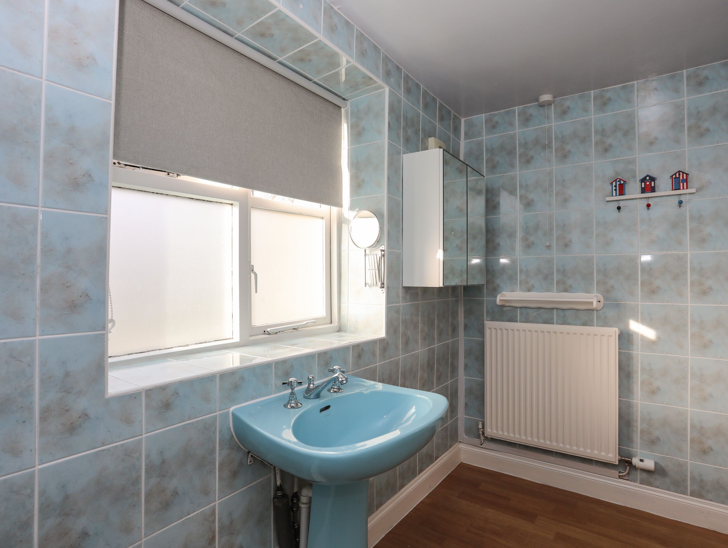 A bathroom with a blue sink, a window with a blind, a mirror, a towel rack, and a radiator.