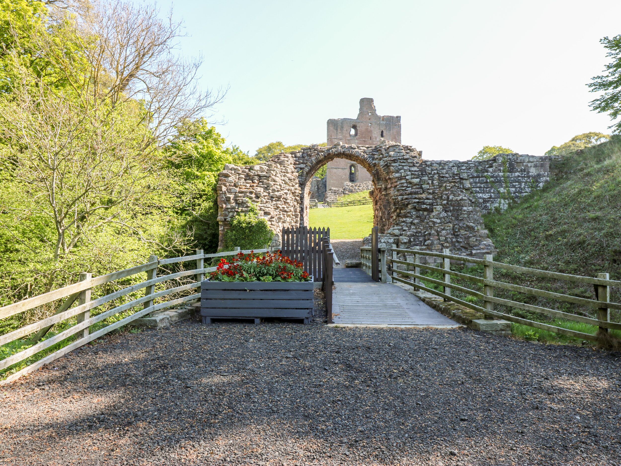 A stone archway leading to a castle ruin with a gravel path and wooden fence.