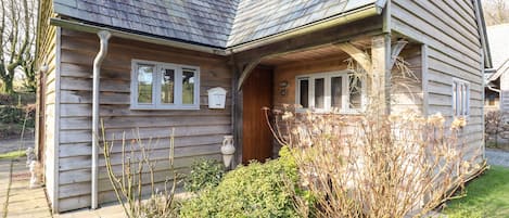 A wooden house with a sloped roof, a front porch, and a small garden area with various plants.