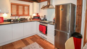 Eine moderne Küche mit weißen Schränken, einem Edelstahl-Kühlschrank, einer Mikrowelle und Holzbalken an der Decke.