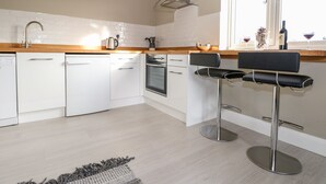 Ett modernt kök med vita skåp, en fläktkåpa i rostfritt stål, en inbyggd ugn och ett fönster med utsikt över omgivningen.