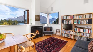 Uma sala de estar com lareira, estante de livros, sofá e um espaço de jantar com cadeiras e mesa.