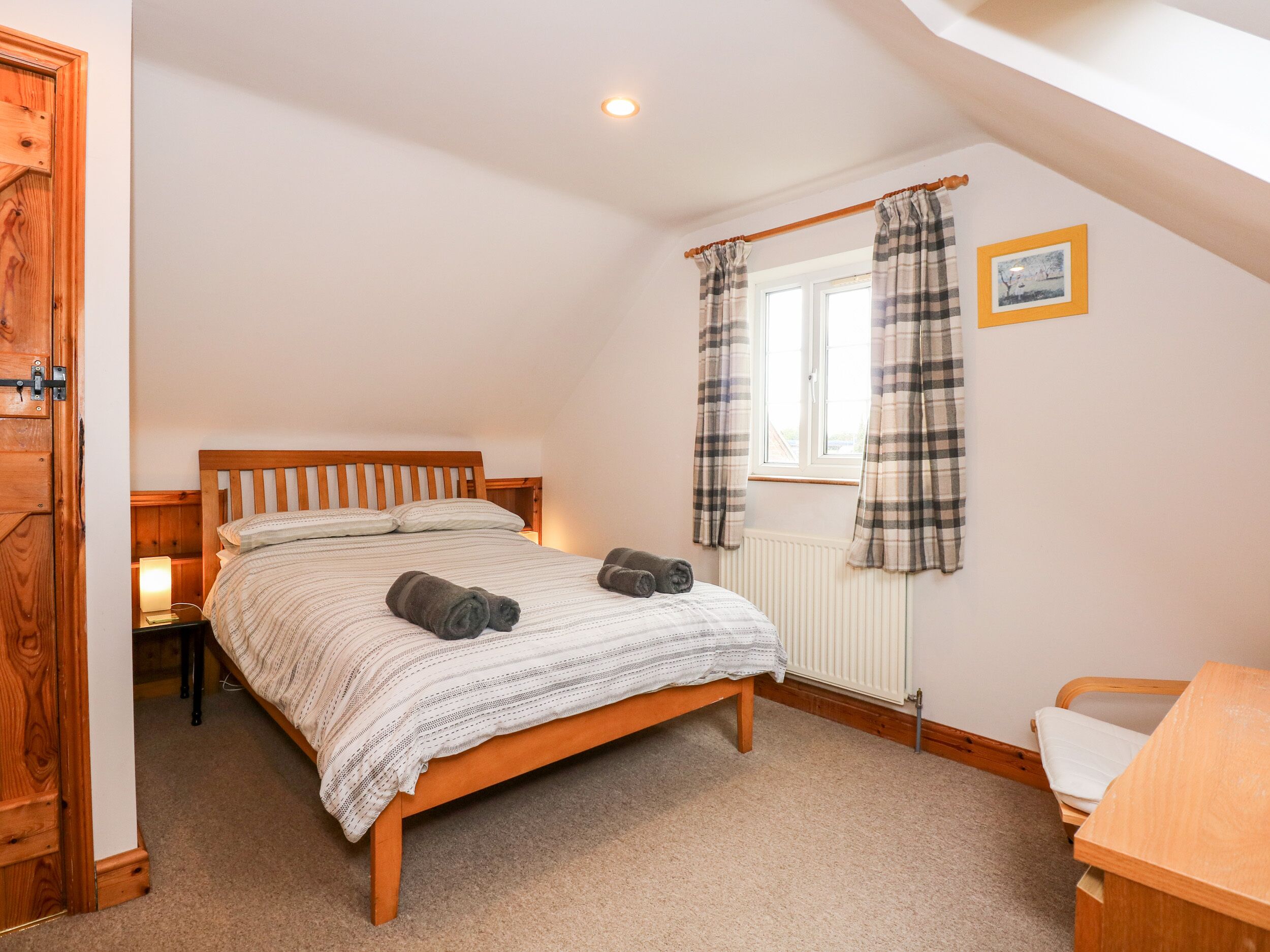 A bedroom with a wooden bed, a nightstand, a window with curtains, a radiator, and a small desk.