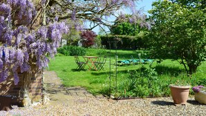 A garden with a brick wall, a table with chairs, and a variety of plants. - Wisteria Cottage (King's Lynn)