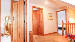 A room with wooden doors, a mirror, a small table with a vase, and a painting on the wall. - Wisteria Cottage (King's Lynn)