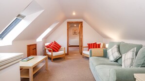A cozy attic bedroom with a sloped ceiling, a wooden bed, a green sofa, and a small table with books. - Wisteria Cottage (King's Lynn)