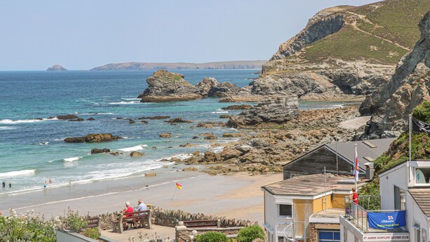 A coastal beach with rocky terrain, a lifeboat station, and a building with a sign for a surf life-saving club. - 3 Rose Cottages (St. Agnes)