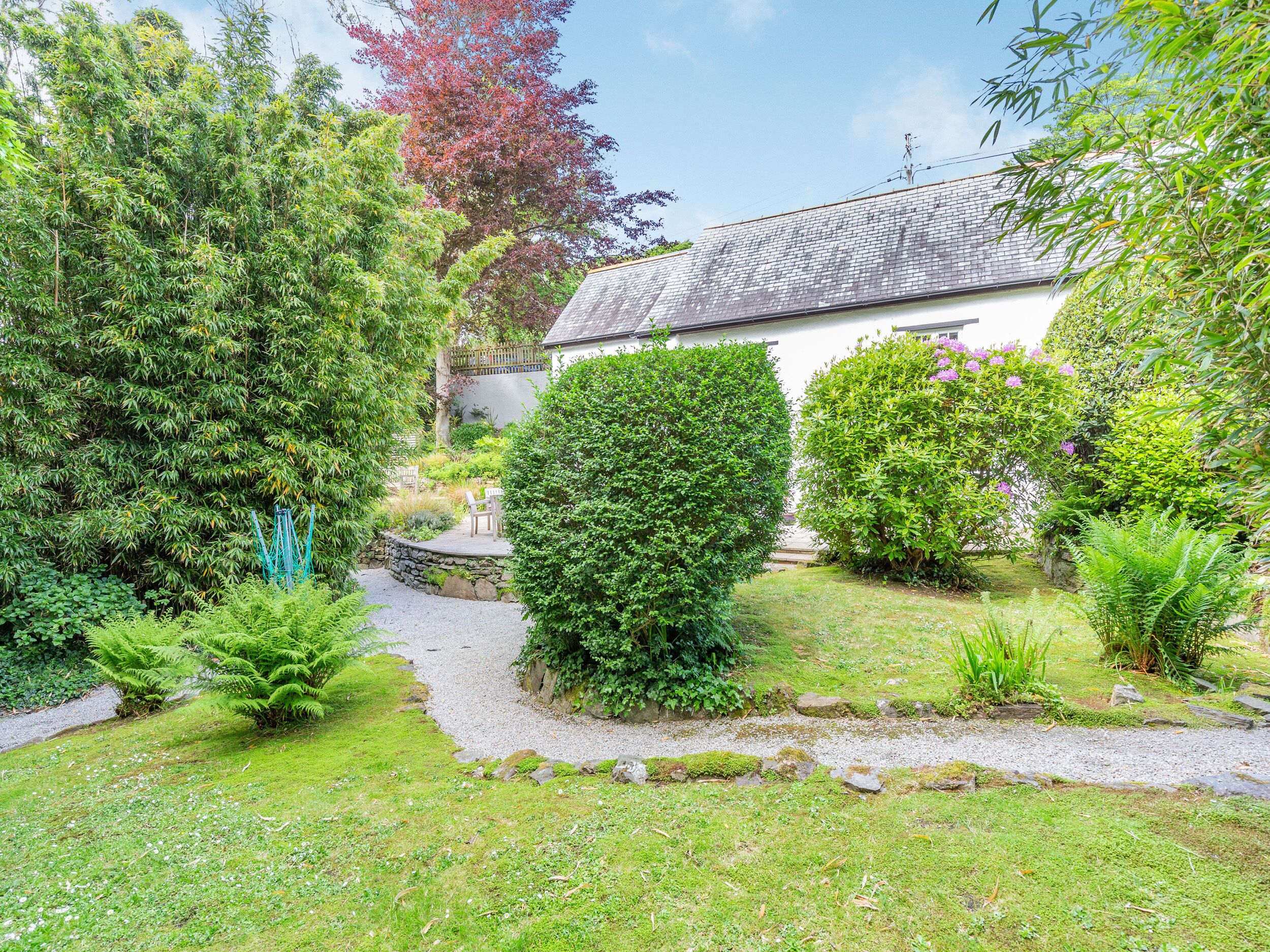 A garden with a stone pathway leading to a white building with a grey roof.