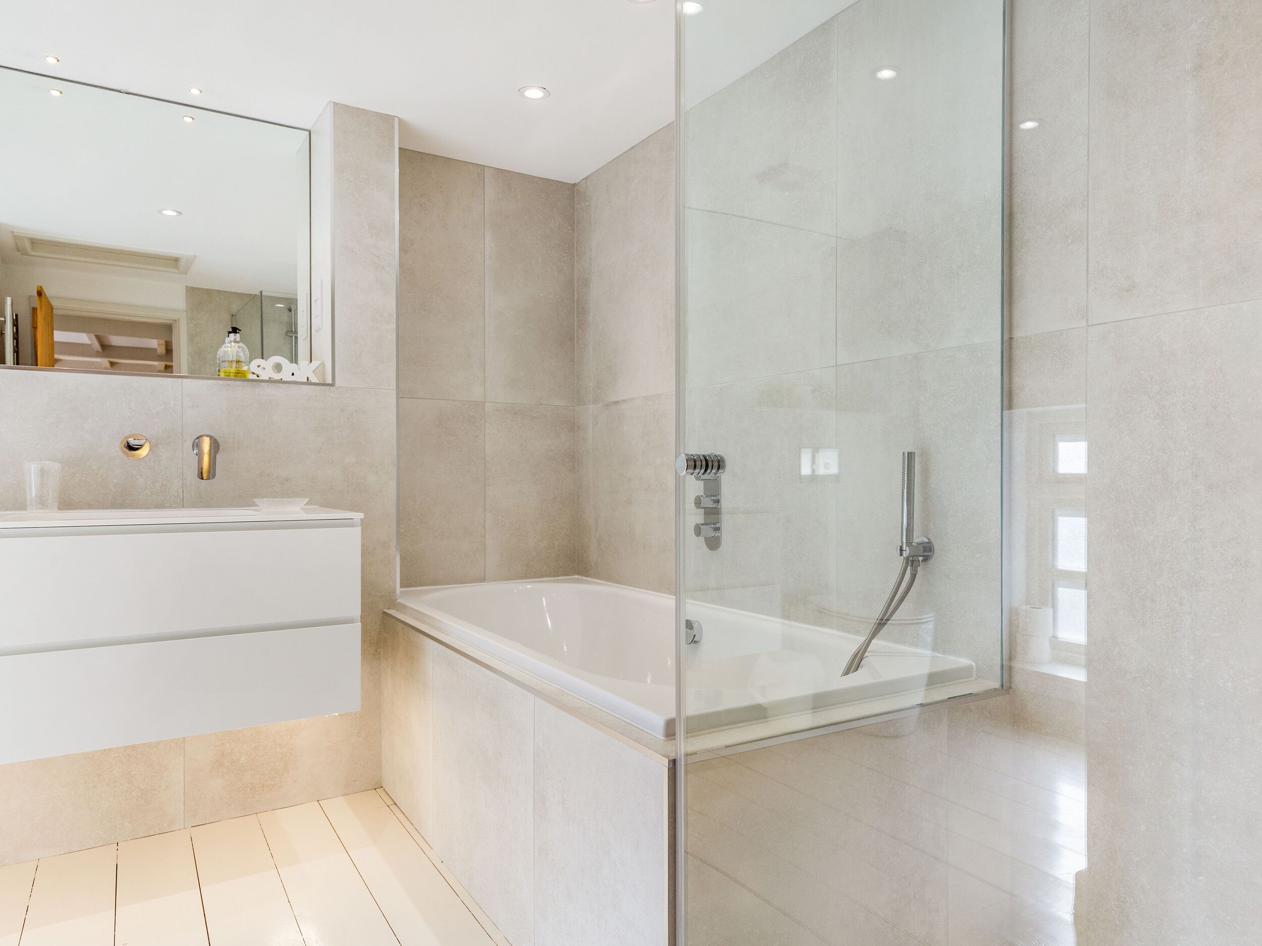 A modern bathroom with a glass-enclosed shower, a white bathtub, and a vanity with a mirror.