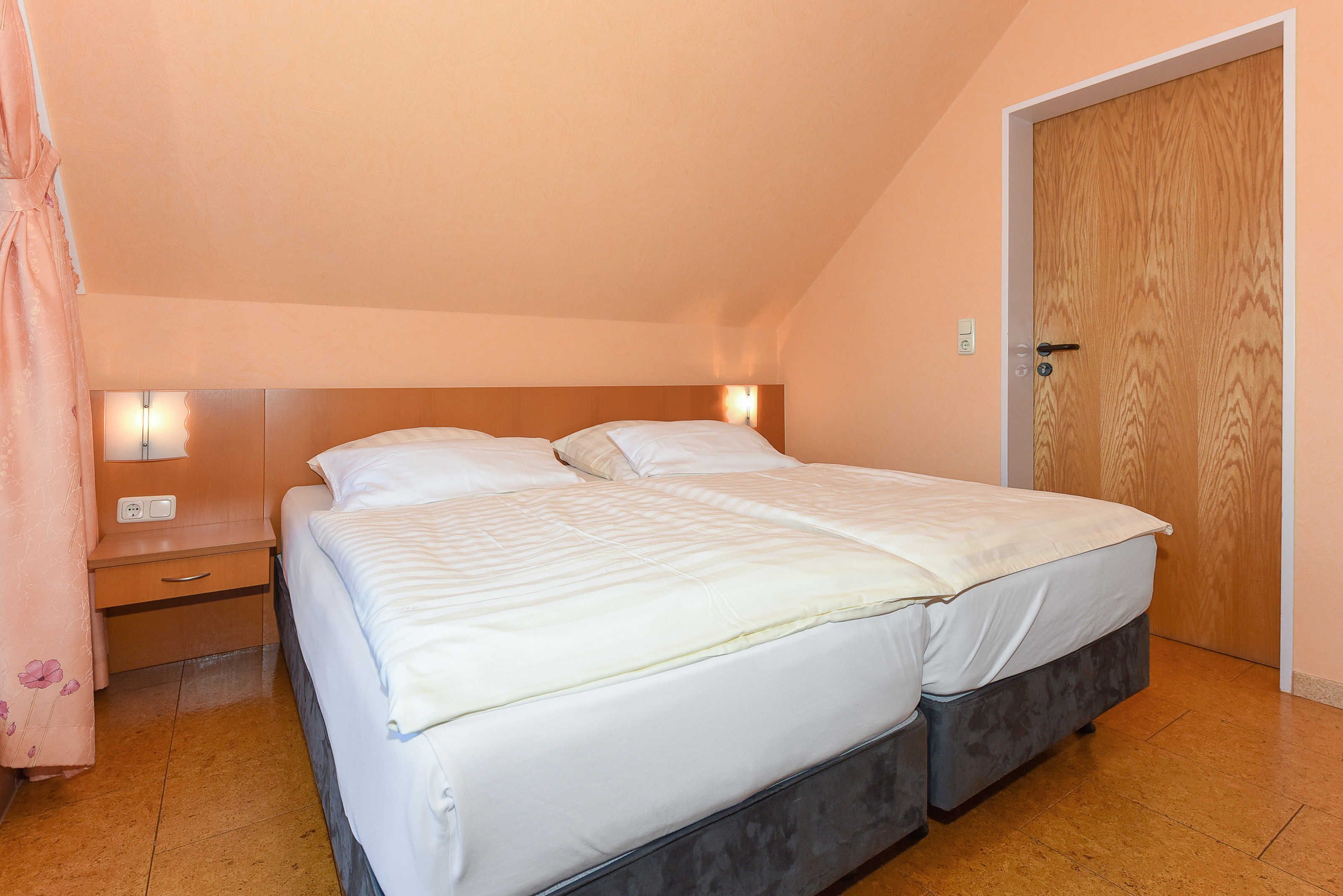 Une chambre à coucher avec un lit double, une table de chevet, une porte en bois et un interrupteur sur le mur.