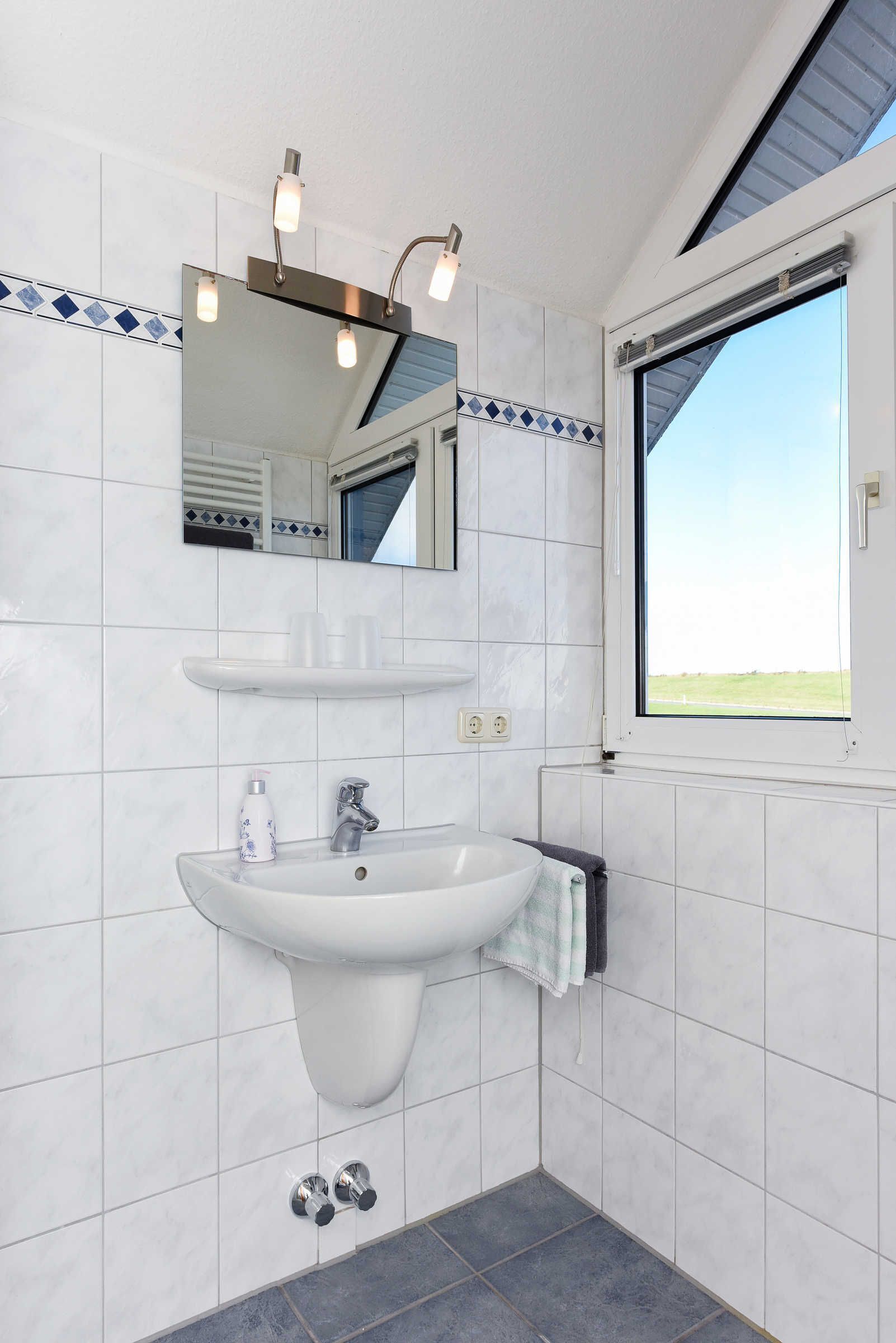 Ein Badezimmer mit einem weißen Waschbecken, einem Spiegel und einem Fenster.