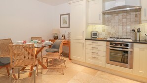 A modern kitchen with white cabinets, a gas stove, and a microwave. There is a dining table with chairs and a lamp on the side. - East Newk Cottage (Bridlington)