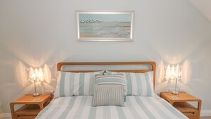 A neatly made bed with striped bedding, two bedside tables with lamps, and a framed painting above the bed. - East Newk Cottage (Bridlington)