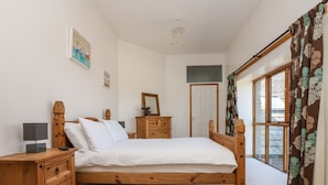 Un dormitorio con cama de madera, una mesita de noche, cómoda, espejo y ventana con cortinas.