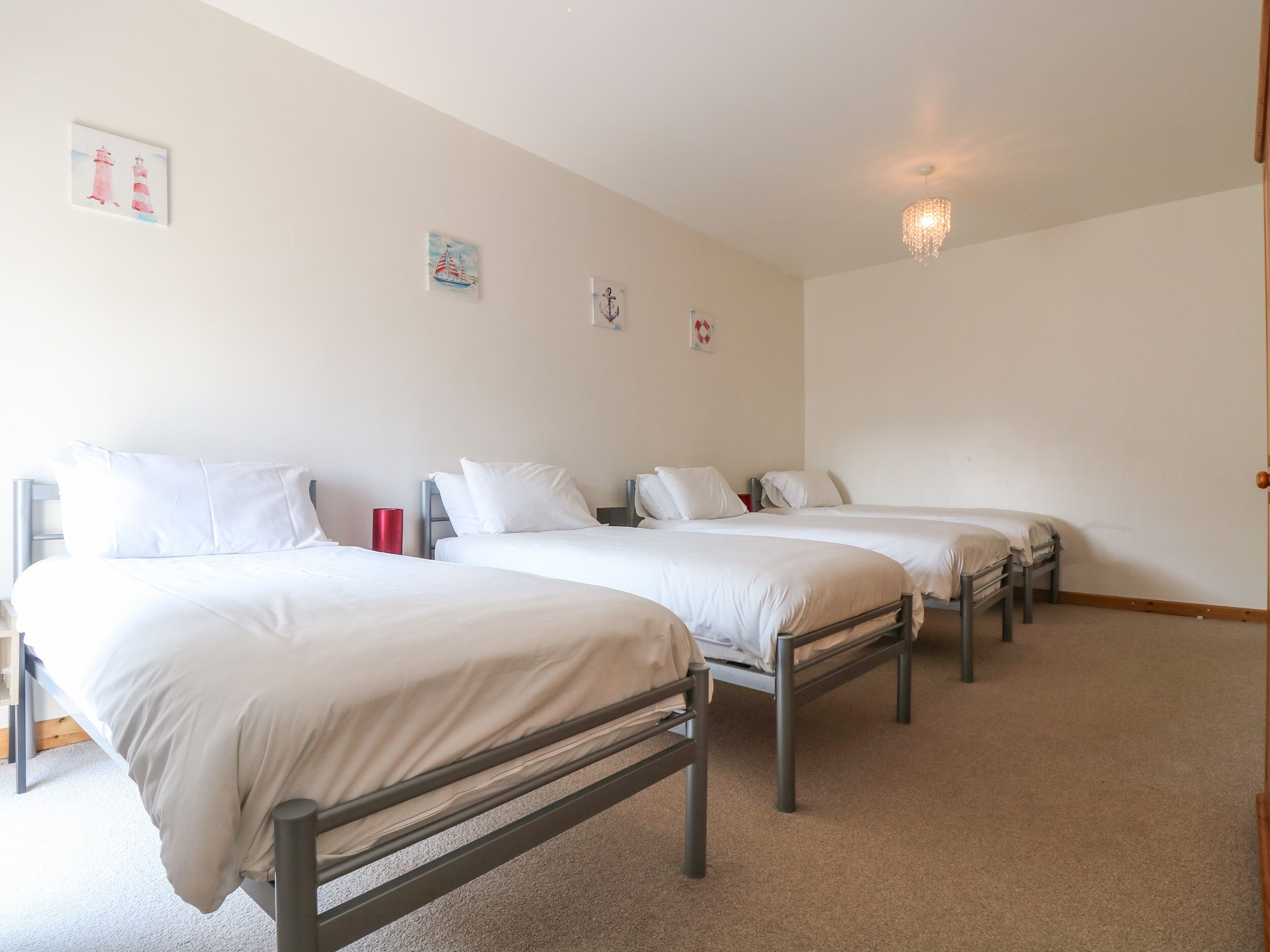 A hotel room with three single beds, a red cylindrical object on the nightstand, and a chandelier.