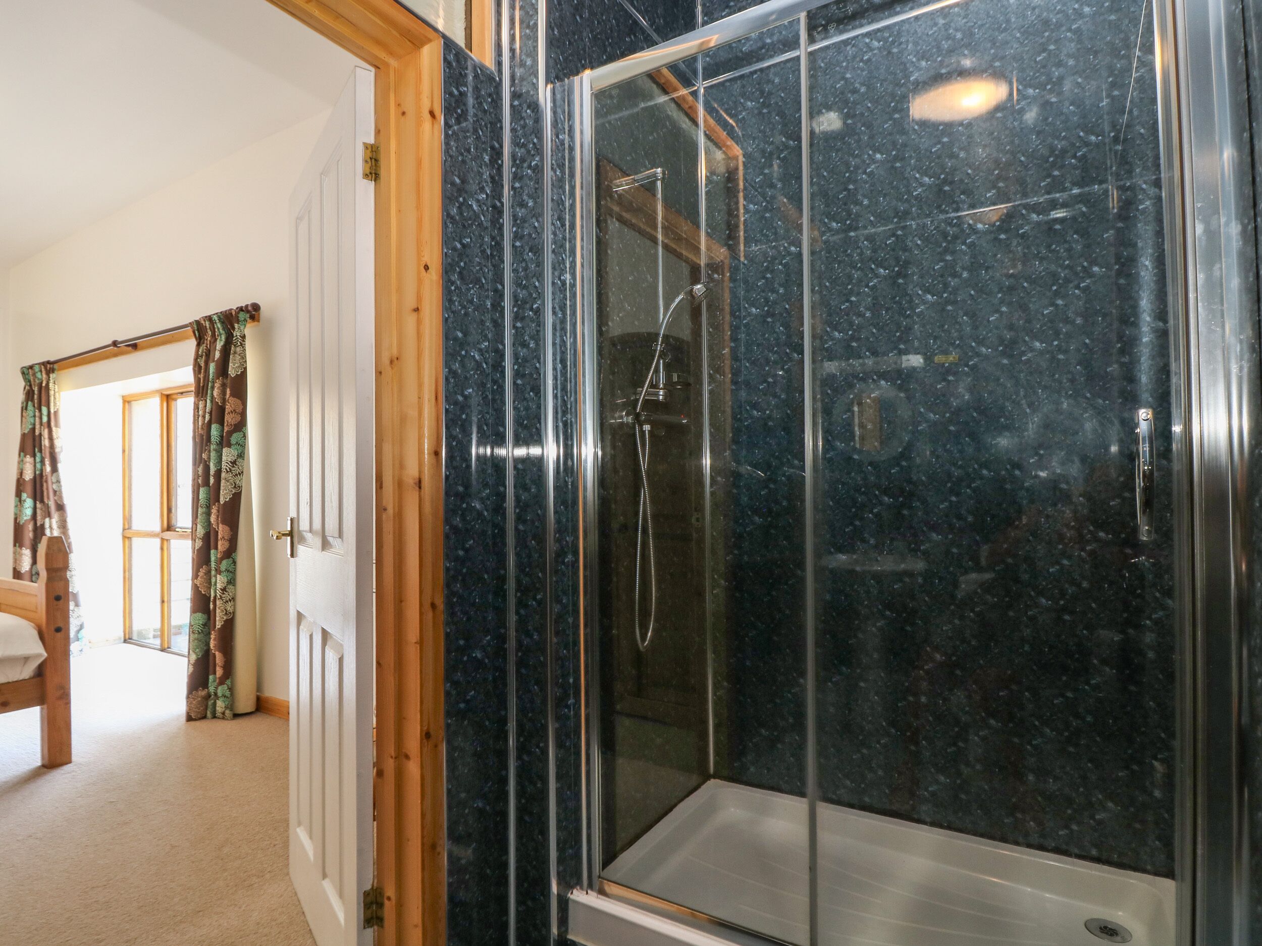 A modern bathroom with a glass-enclosed shower, wooden door frame, and a visible toilet.