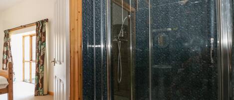 A modern bathroom with a glass-enclosed shower, wooden door frame, and a visible toilet.