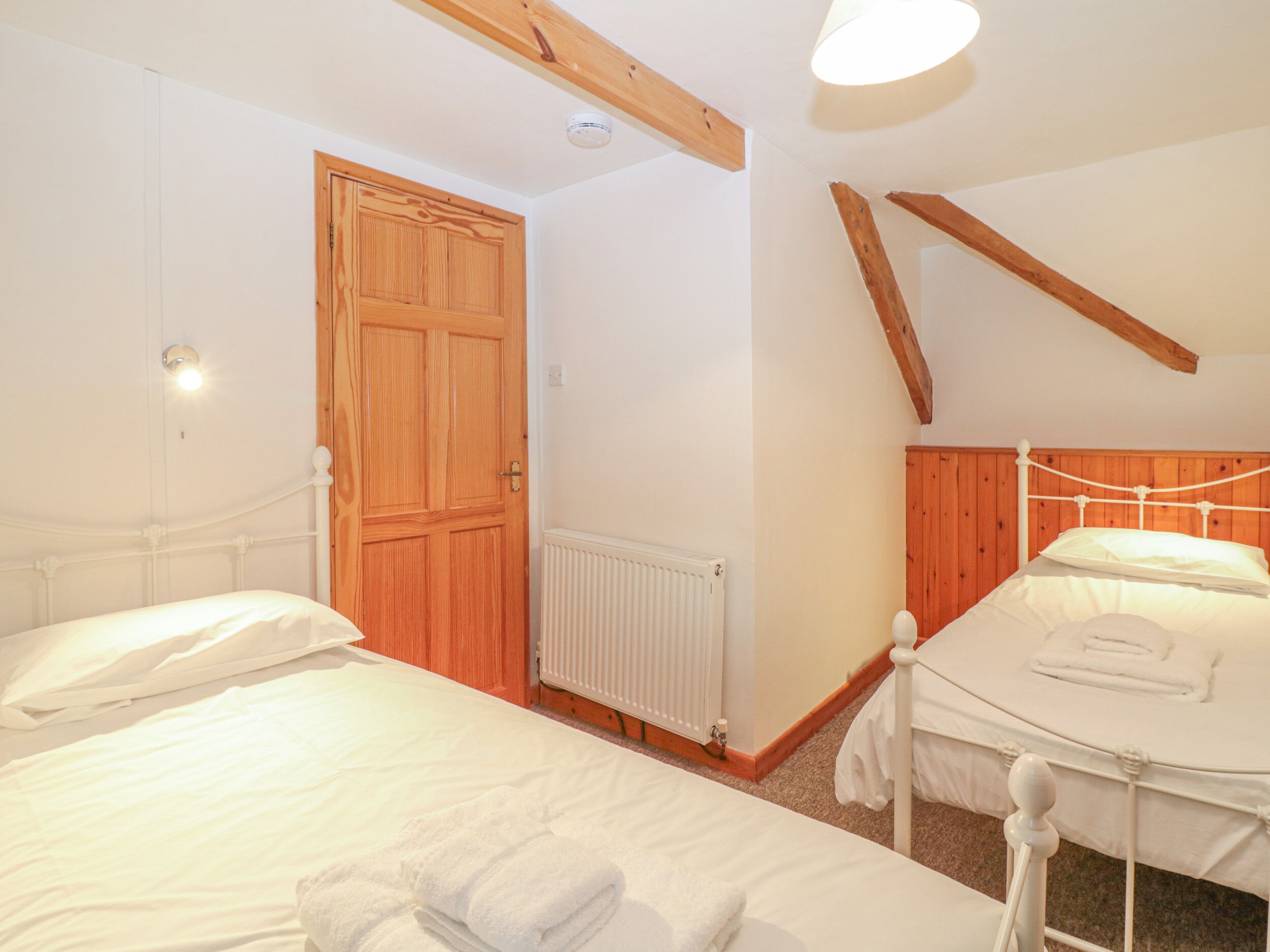 A bedroom with two beds, wooden beams, a radiator, and a wooden door.