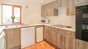 A modern kitchen with wooden cabinets, a dishwasher, a microwave, and an oven. - The Wagon Linney (Bude)