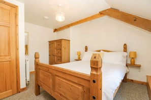 Una cama de madera con dos mesitas de noche, un armario de madera y una lámpara en el techo en una habitación con paredes blancas y techo inclinado.