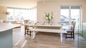 Un'ampia sala da pranzo con un lungo tavolo apparecchiato per quattro persone, ampie finestre con vista sulla città e un design d'interni moderno.