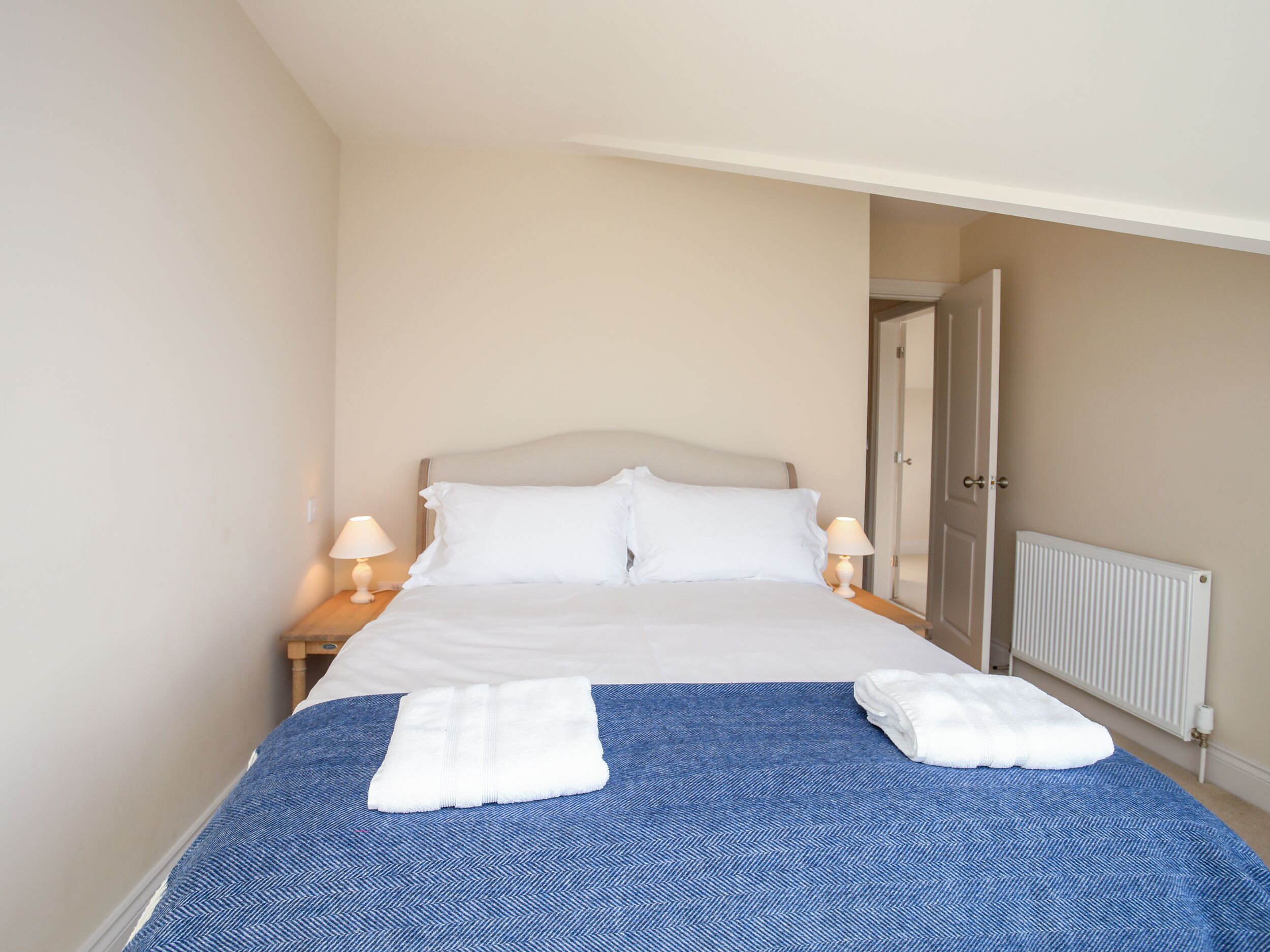 Un lit bien fait, avec du linge de lit blanc, deux serviettes blanches pliées sur le lit et une couvre-lit bleue à motifs chevrons.