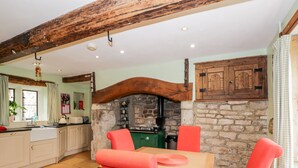 A kitchen with a stone wall, wooden beams, a green stove, and a wooden cabinet. - Chapel House (Stonehouse)