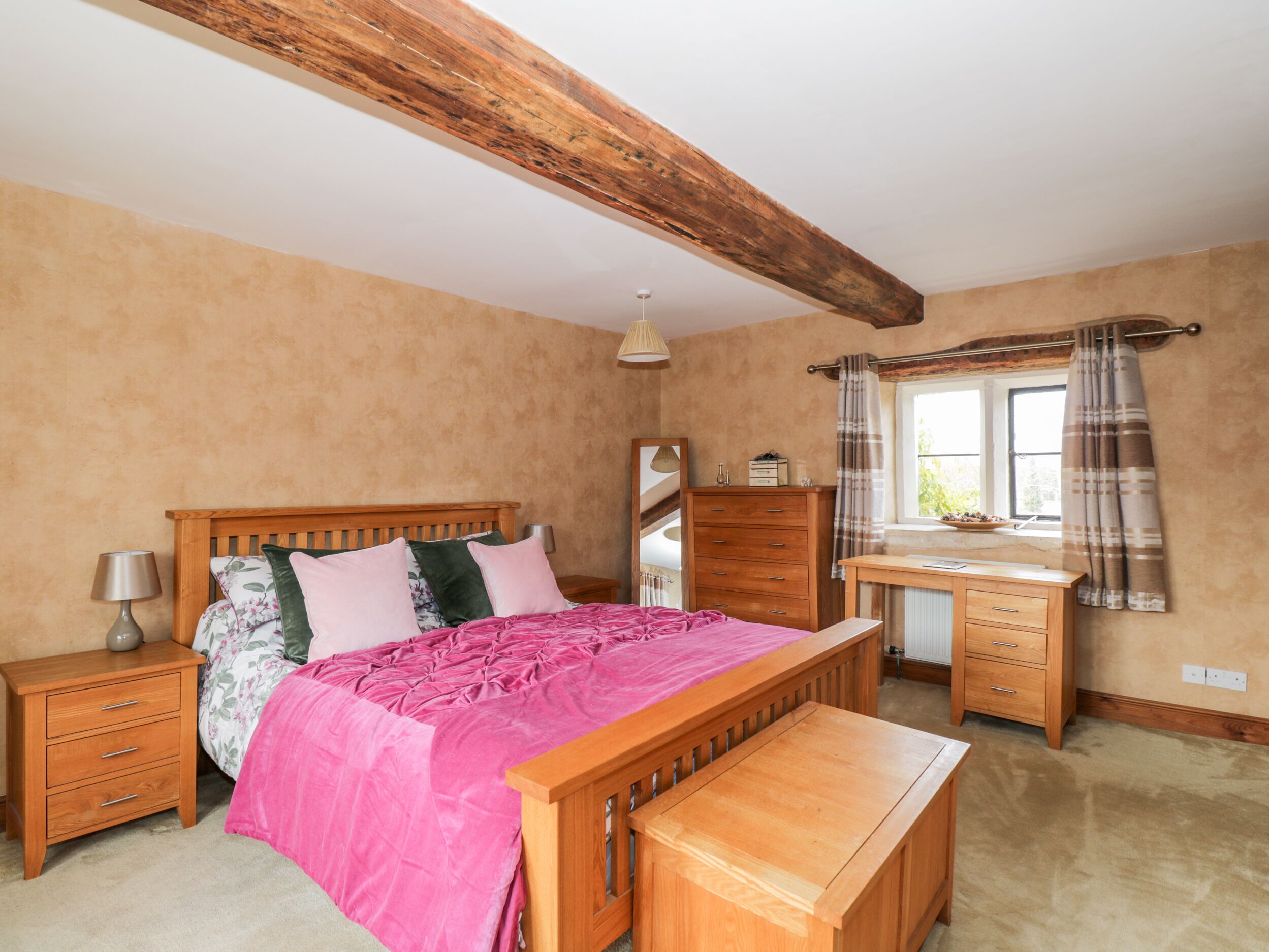 A bedroom with a wooden bed, bedside tables, a dresser, and a window with curtains.
