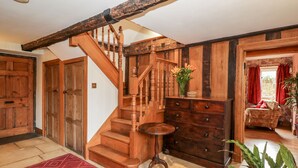 A wooden staircase with a round table and a vase of flowers, leading to a room with a patterned rug and a wooden dresser. - Chapel House (Stonehouse)