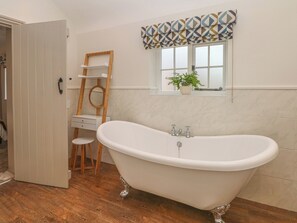 A bathroom with a freestanding bathtub, a wooden ladder, a small window with a patterned valance, and a potted plant on the windowsill. - Lakeside Cottage (Macclesfield)