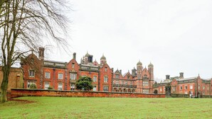 A large, historic red brick building with multiple towers and a well-maintained lawn in front. - Lakeside Cottage (Macclesfield)