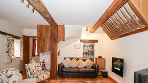 A cozy living room with a wooden ceiling, a fireplace, a bookshelf, and a comfortable sofa. - Chapel Cottage (Stonehouse)
