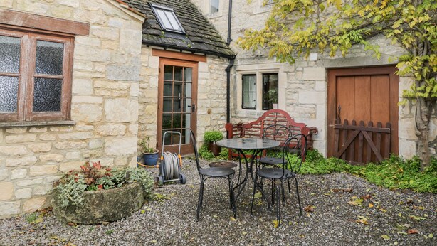 A stone building with a wooden door, a window, and a small garden area with a table and chairs. - Chapel Cottage (Stonehouse)