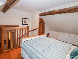 Un dormitorio con una escalera de madera, una cama con cubrecama a rayas, un radiador y un extintor.