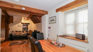 A cozy living room with a wooden dining table, leather chairs, and a bookshelf. - Chapel Cottage (Stonehouse)