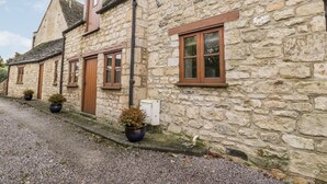 A stone building with a gravel driveway, wooden doors, and potted plants. - Chapel Cottage (Stonehouse)