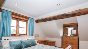 A bedroom with a bed, a dresser, a mirror, and a window with curtains. - Chapel Cottage (Stonehouse)