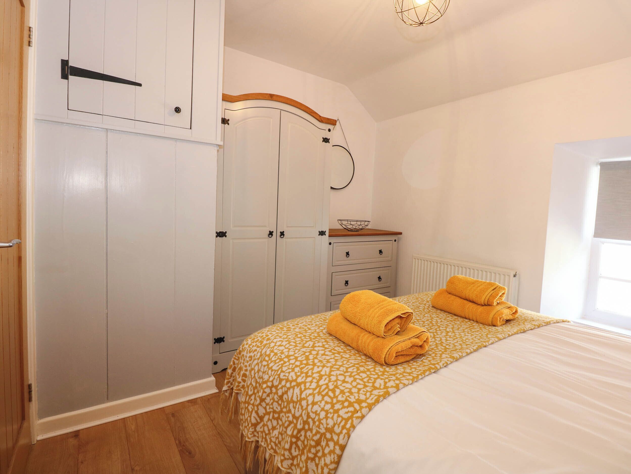 A bedroom with a bed, two white wardrobes, a wooden dresser, and a window with a view.