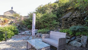 Un jardin avec un mur de pierre, un banc en bois et une table.