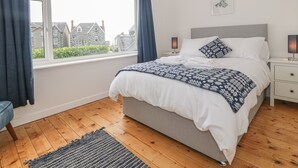 Un dormitorio ordenado con una cama grande, una mesita de noche con lámparas, vistas al exterior a través de una ventana y un cuadro en la pared.