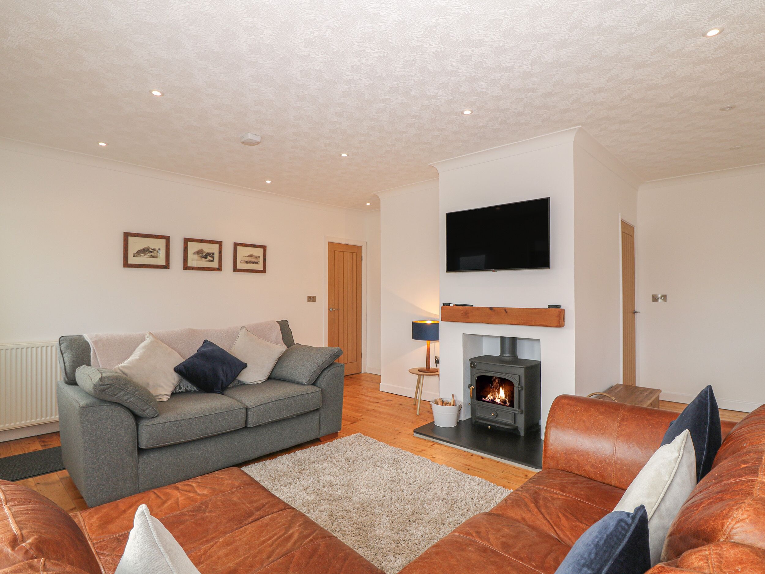 A living room with a grey sofa, a brown leather sofa, a fireplace, a television mounted on the wall, and framed pictures on the wall.
