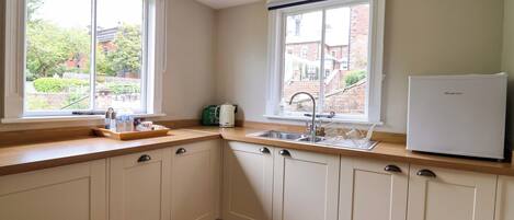 A kitchen with two windows, a sink, a kettle, and a refrigerator.